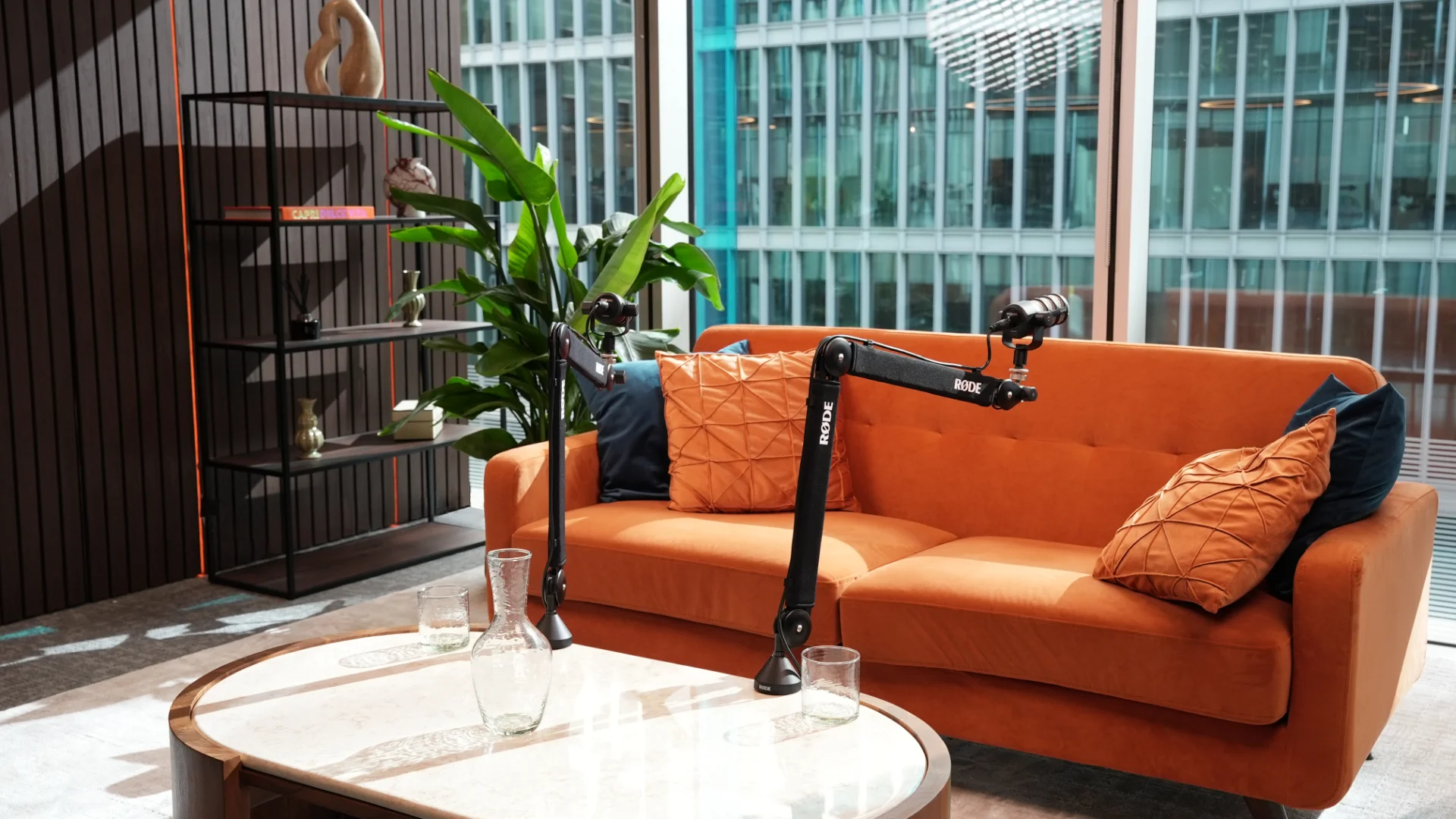 The orange sofa and microphones in daylight, with the office towers through the windows